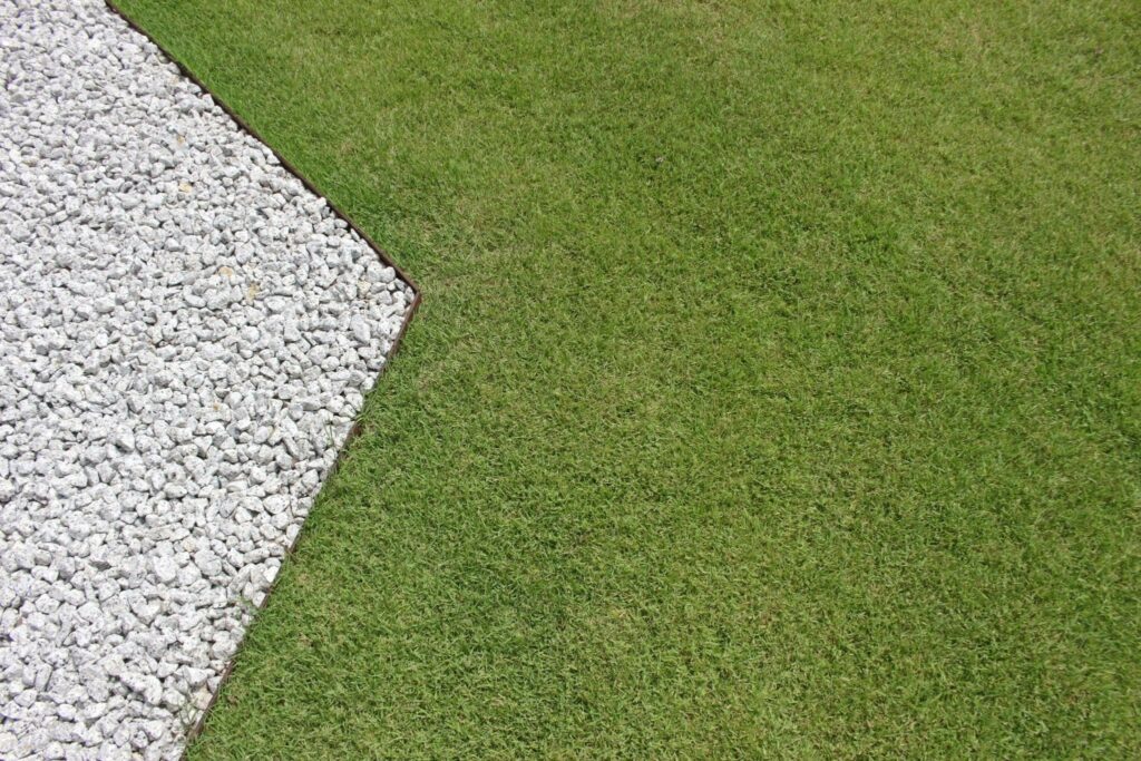 closeup of a crisp, angular border dividing a green lawn from a bed of white landscape rocks.