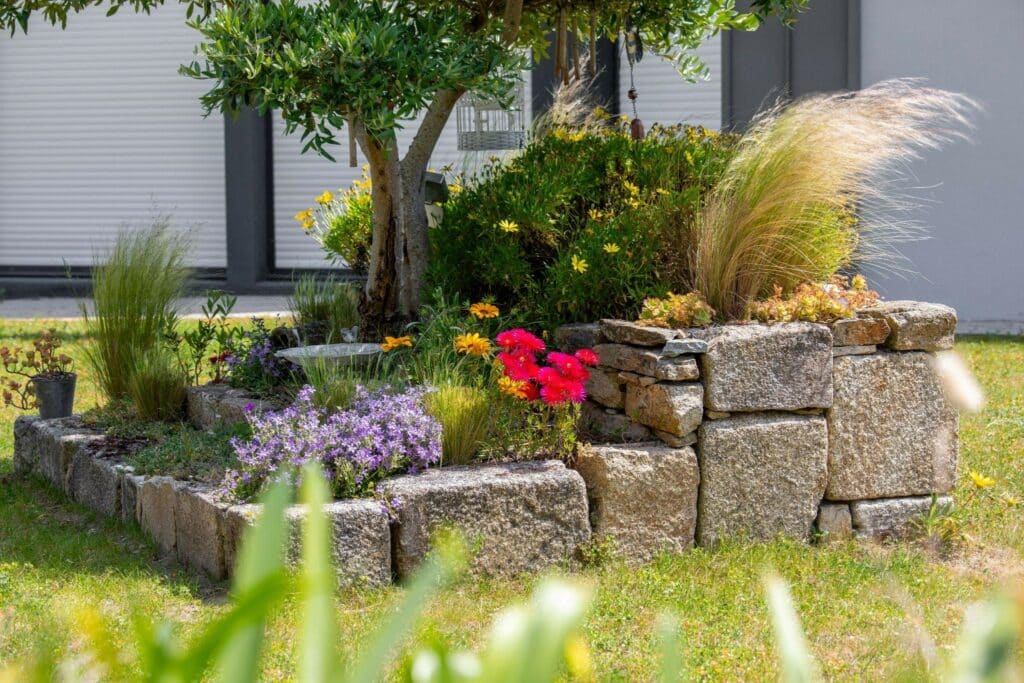 hand-built natural stone planters with flowers and grasses in a backyard under a tree