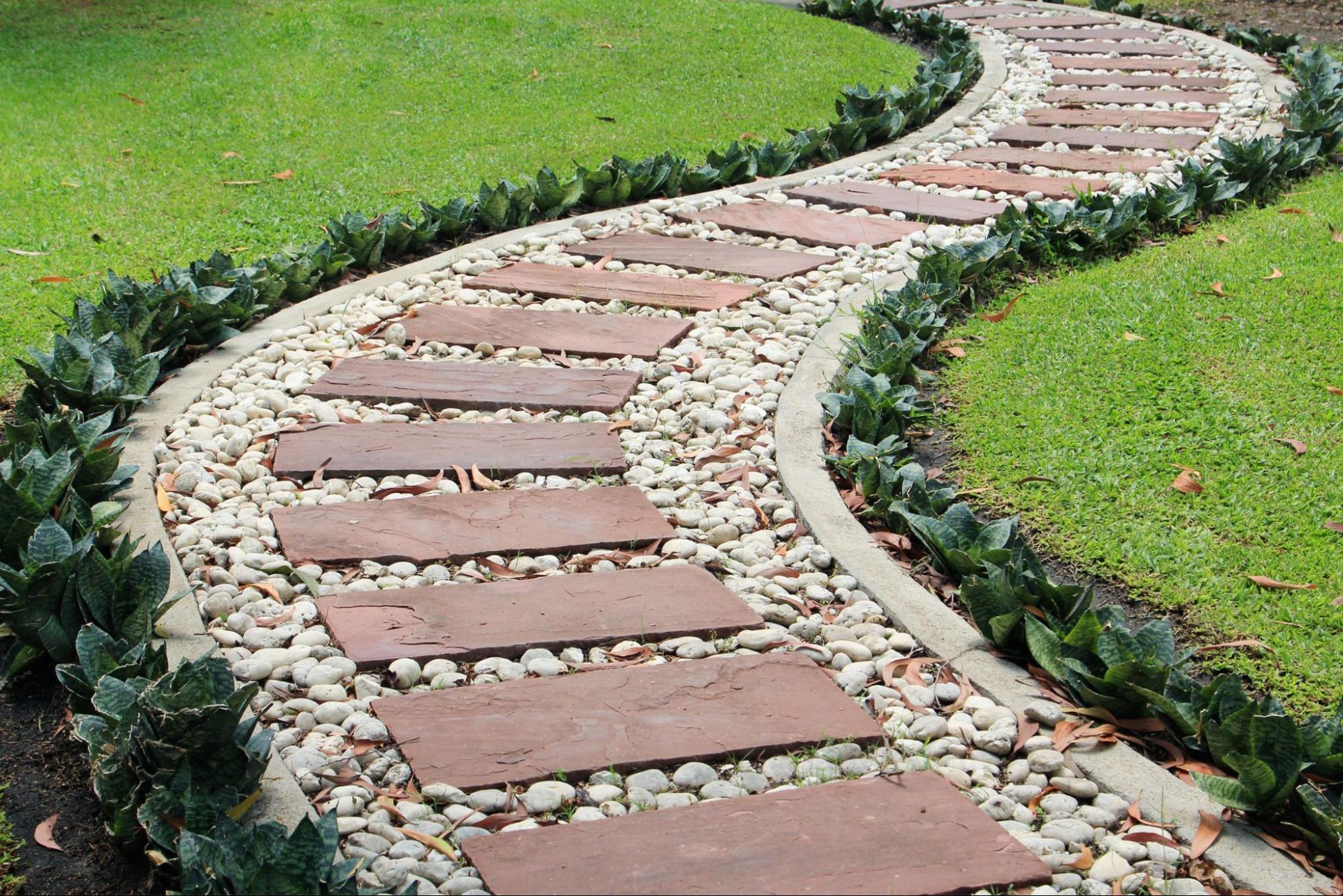 A path with reddish flagstone steps surrounded by pea gravel and lined with a plant border.